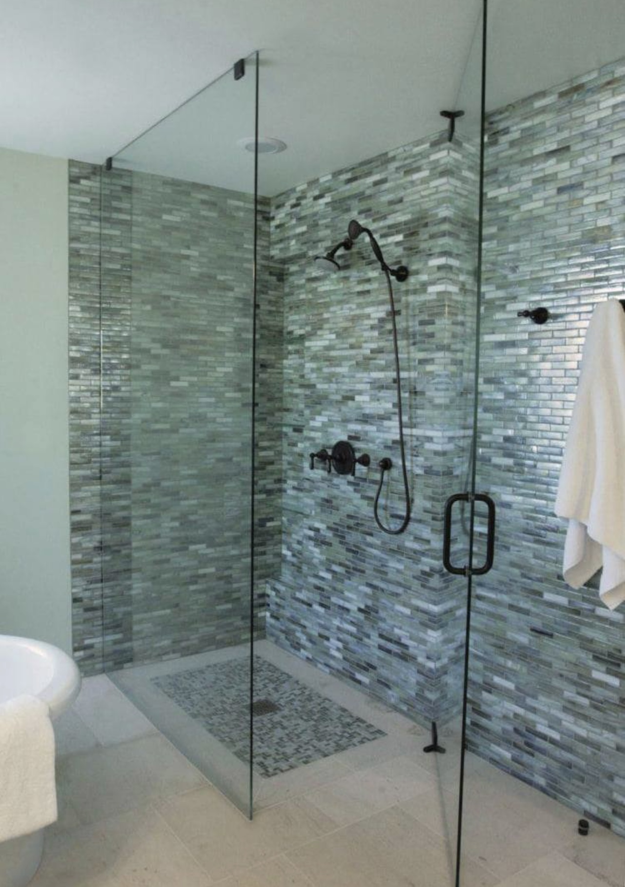 Green mosaic tilework in a glass enclosed shower